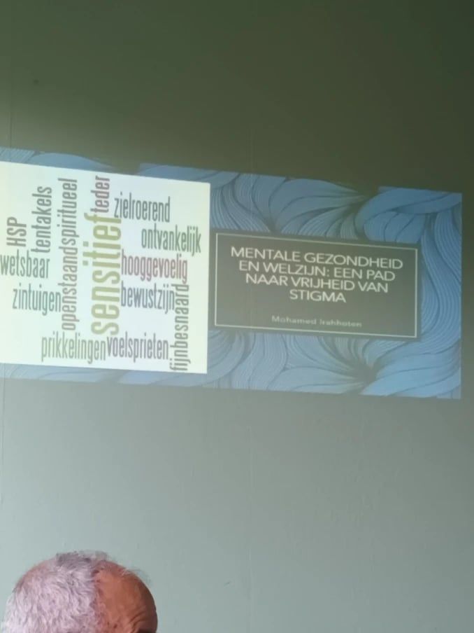 Een geprojecteerde dia met de titel Mentale gezondheid en welzijn: een pad naar vrijheid van stigma, naast een woordwolk met woorden als sensitief, hooggevoelig en kwetsbaar.