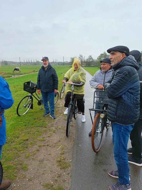 Deelnemers met fietsen op een pad door de weilanden, een van hen in een gele regenponcho.